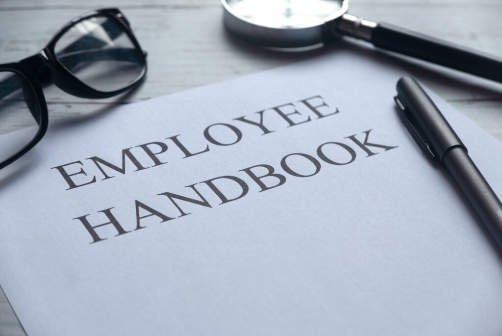 Selective focus of glasses, magnifying glass, pen and paper written with Employee Handbook on white wooden background.