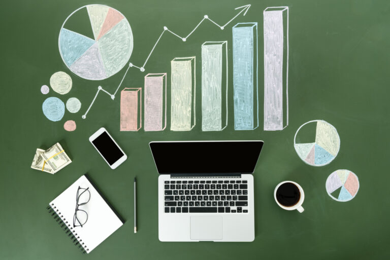 Top view of laptop and business charts with cup of coffee and smartphone on a green background.